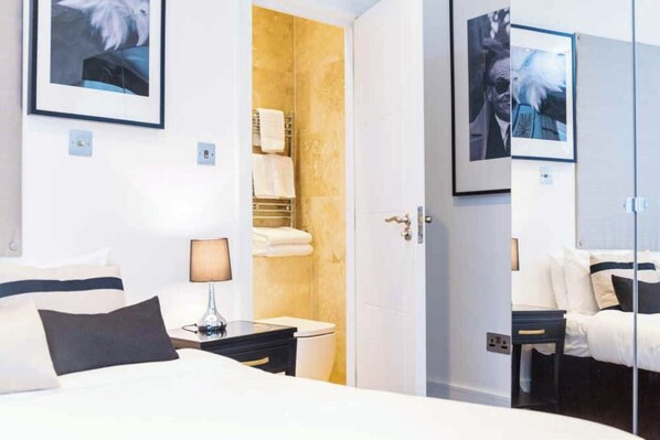 Une chambre d’hôtel avec un lit, une table de chevet, une lampe et une salle de bain visible à travers une porte ouverte.