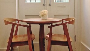 A dining area with a round table and two wooden chairs, a small vase with flowers, and a white door with glass panels.
