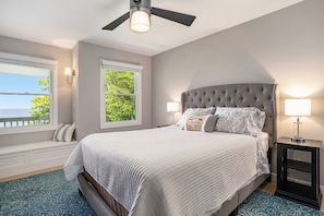 A bedroom with a large bed, two bedside lamps, a ceiling fan, and a window with a view.
