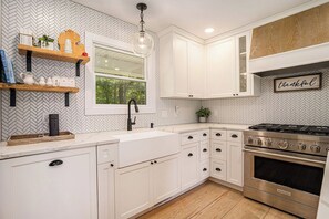 A kitchen with white cabinetry, a herringbone-patterned backsplash, a window, and a stainless steel stove.