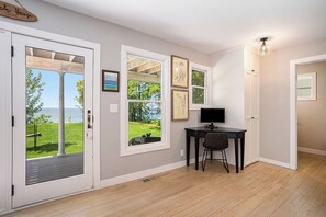 A room with a desk, chair, and a view of a garden and water outside.