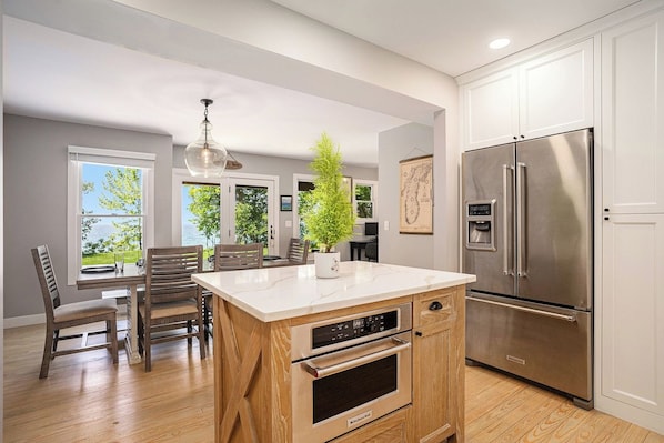 A modern kitchen with a built-in oven, a stainless steel refrigerator, and a dining area with wooden chairs.