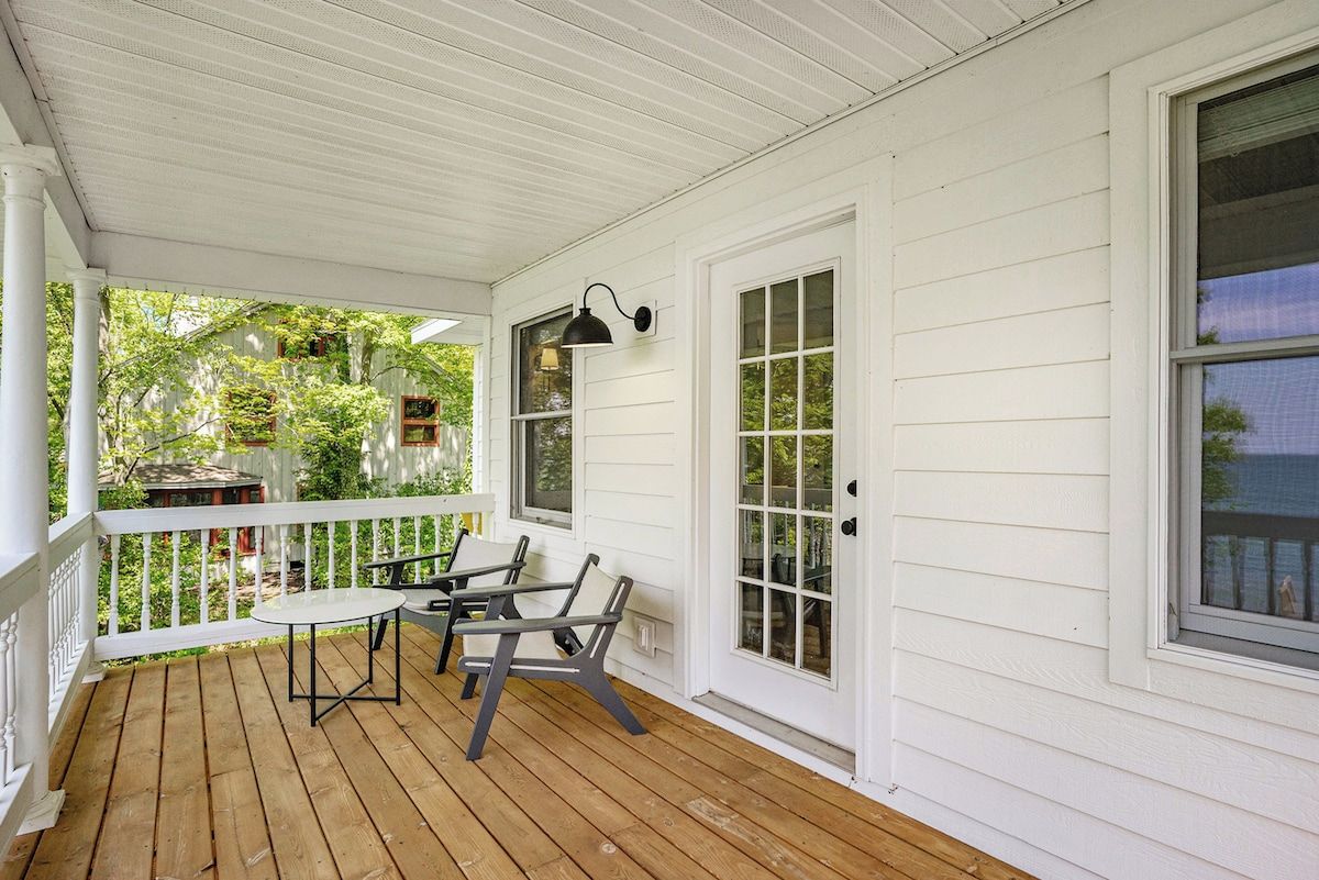 A covered porch with a table and chairs, white siding, and a window.