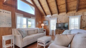 Una sala de estar acogedora con techo de madera, un sofá color beige, una mesa de centro blanca y un televisor.