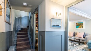 A staircase leading to a closet with a patterned wallpaper, a framed picture on the wall, and a sofa with cushions in a living area.