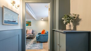 A hallway with a blue door, a blue armchair, a gray armchair, a blue rug, and a vase with green plants.