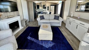 A modern living room with a fireplace, a sofa, a coffee table, and a TV. - Lodge No 20 | Hot Tub |  Stewart's Resort Cameron (Cameron)