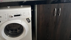 Eine kompakte Küche mit Einbauwaschmaschine, Spüle und dunklen Holzschränken.