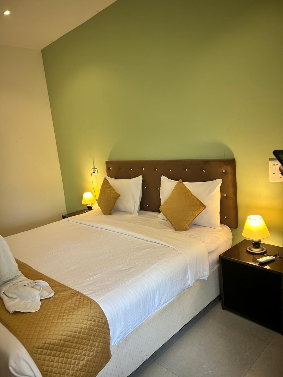 Una habitación de hotel con una cama, dos mesitas de noche y una lámpara.