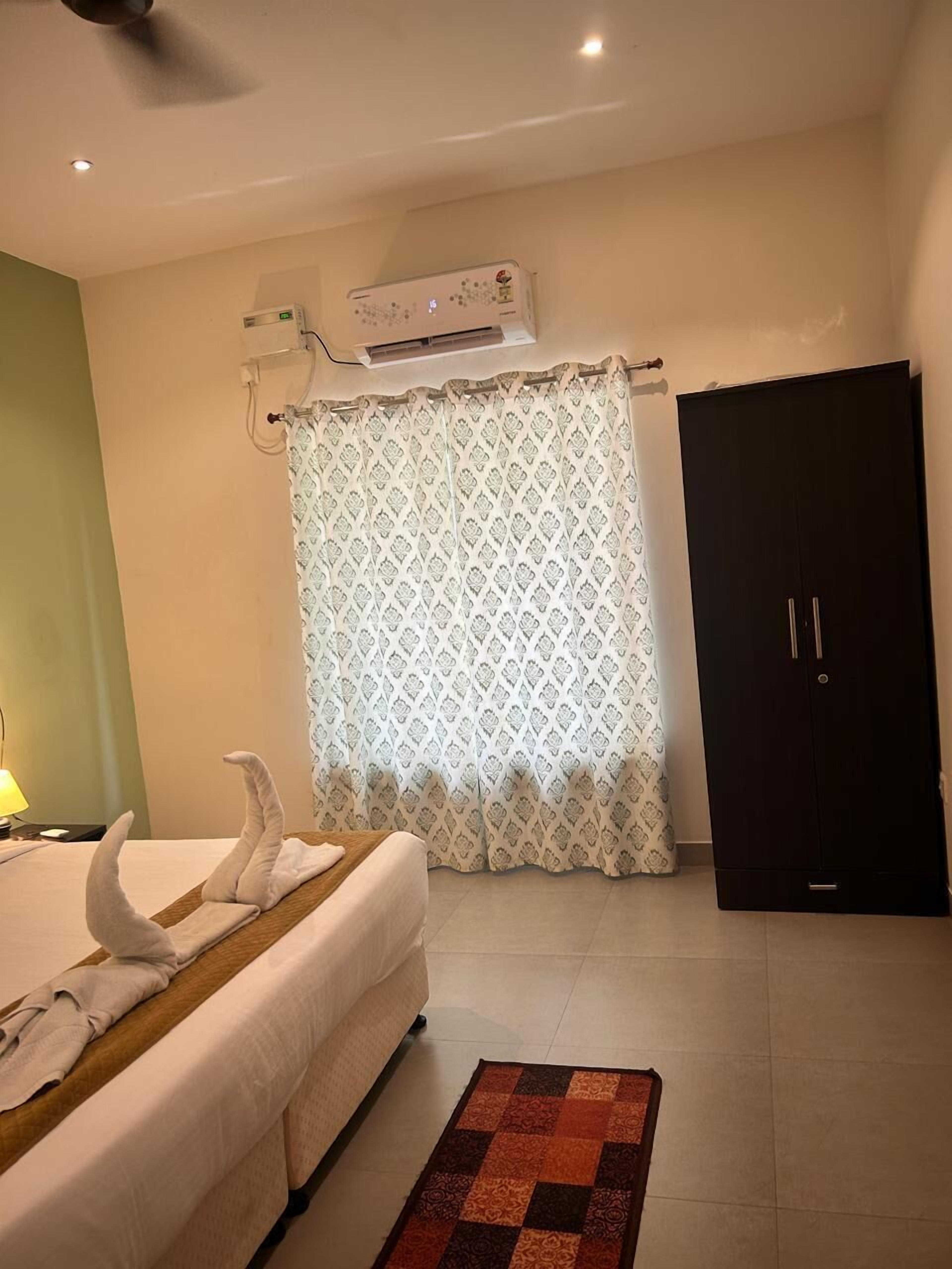 A hotel room with a bed, a black wardrobe, a patterned curtain, and a ceiling fan.