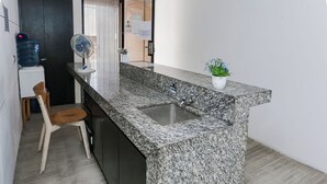 A kitchen with a granite countertop, a sink, a chair, a water dispenser, and a small potted plant. - Hotel O Pondok Indah Near Gandaria City Formerly Odori Residence (Jakarta)
