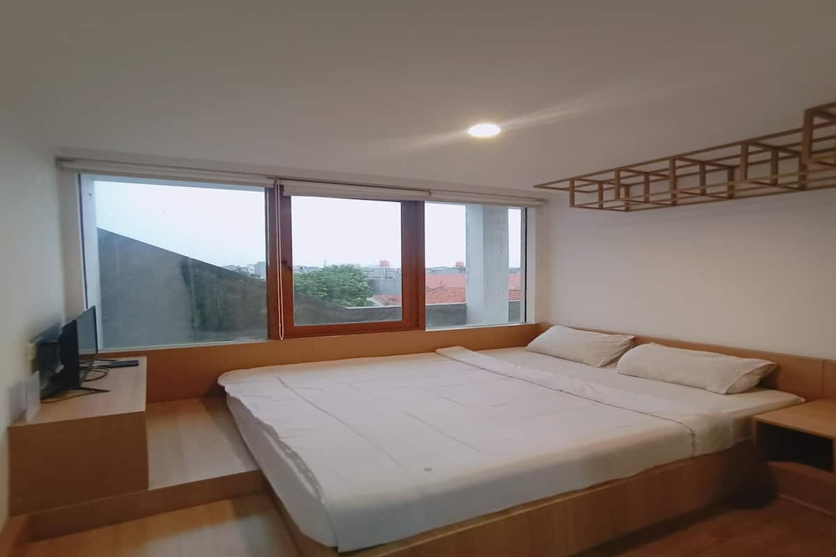 A bedroom with a bed, a TV on a stand, and a window with a view of buildings.