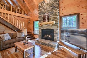 A wooden cabin interior with a stone fireplace, a sofa, a table, and a TV.