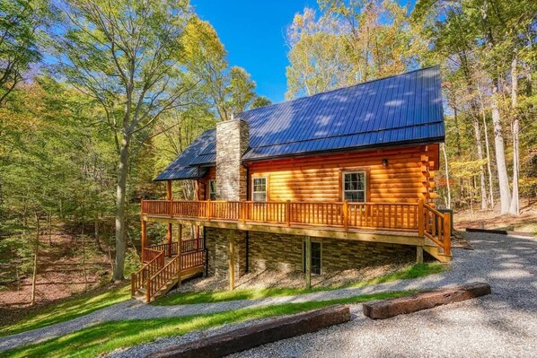 A log cabin with a metal roof, a wooden deck, and a stone chimney.