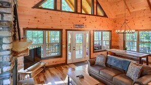 Ein rustikales Blockhaus-Interieur mit Kamin aus Stein, einem Fernseher, einer Couch und großen Fenstern.