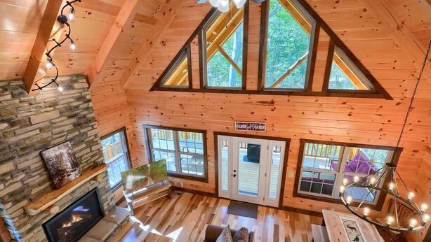 Ein Ferienhausinnenraum mit Kamin aus Stein, Holzböden, Deckenventilator und großen Fenstern.