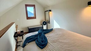 Una camera da letto con un letto, un comodino, una sedia, un termosifone a parete e una finestra vista montagna.