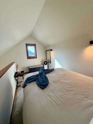 Un dormitorio con cama, mesita de noche, una silla, un calentador de pared y ventana con vistas a la montaña.