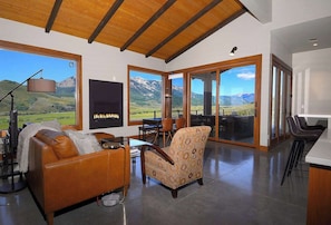 A spacious living area with a fireplace, leather sofa, patterned armchair, and large windows offering mountain views.