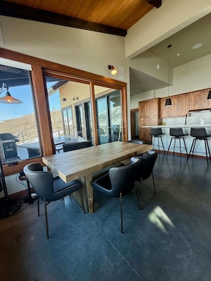 A modern kitchen with wooden cabinets, a large island with bar stools, and large windows offering a view of the outdoors.