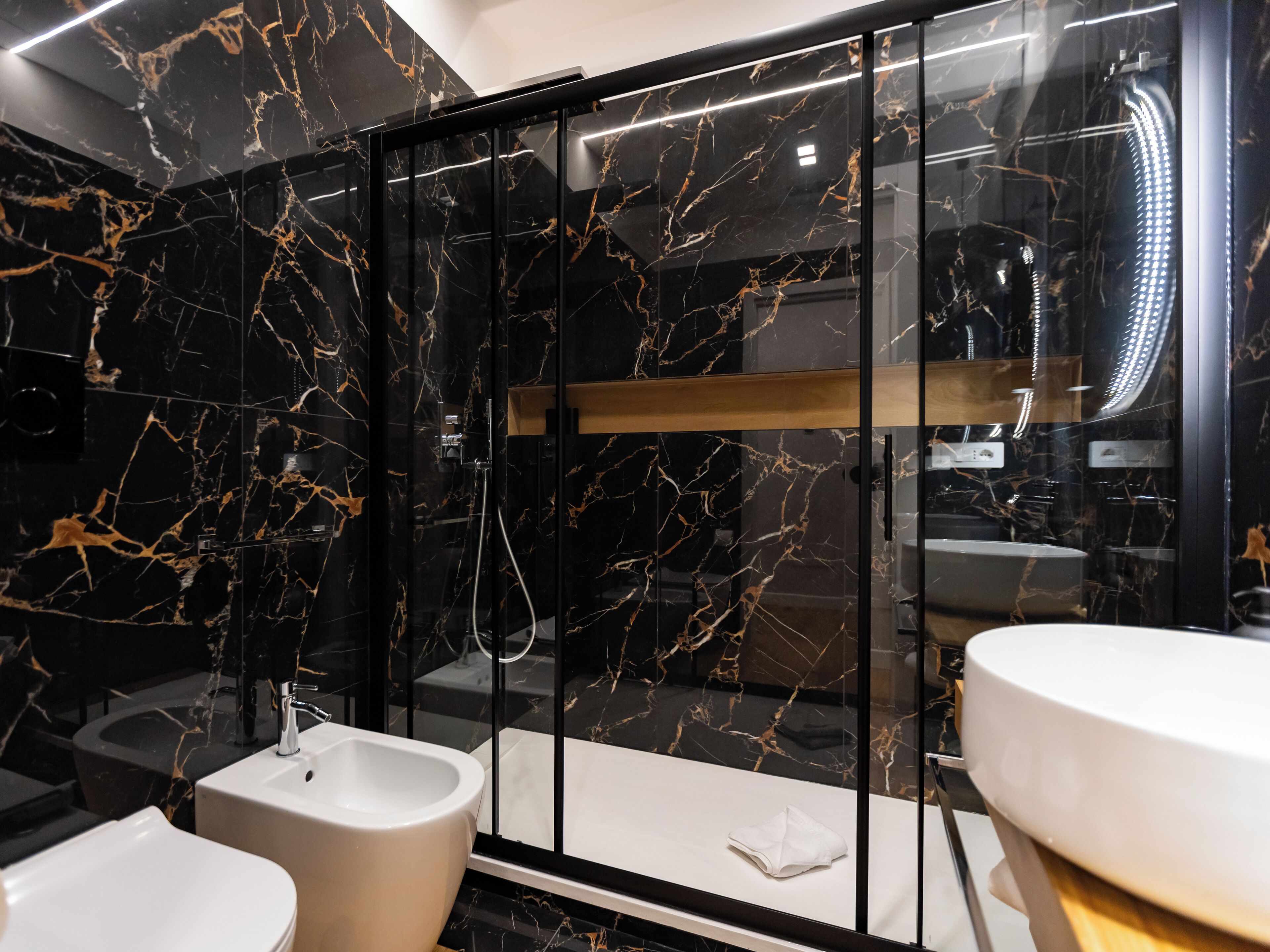 A modern bathroom with black marble walls, a glass-enclosed shower, and two sinks.