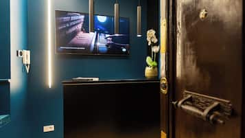 A room with a dark blue wall, a flat-screen TV mounted above a black console, pendant lights, and a door with a brass handle.