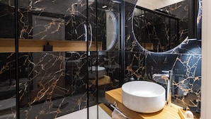 Une salle de bain moderne avec un meuble-lavabo en marbre noir, un lavabo rond et une cabine de douche en verre.