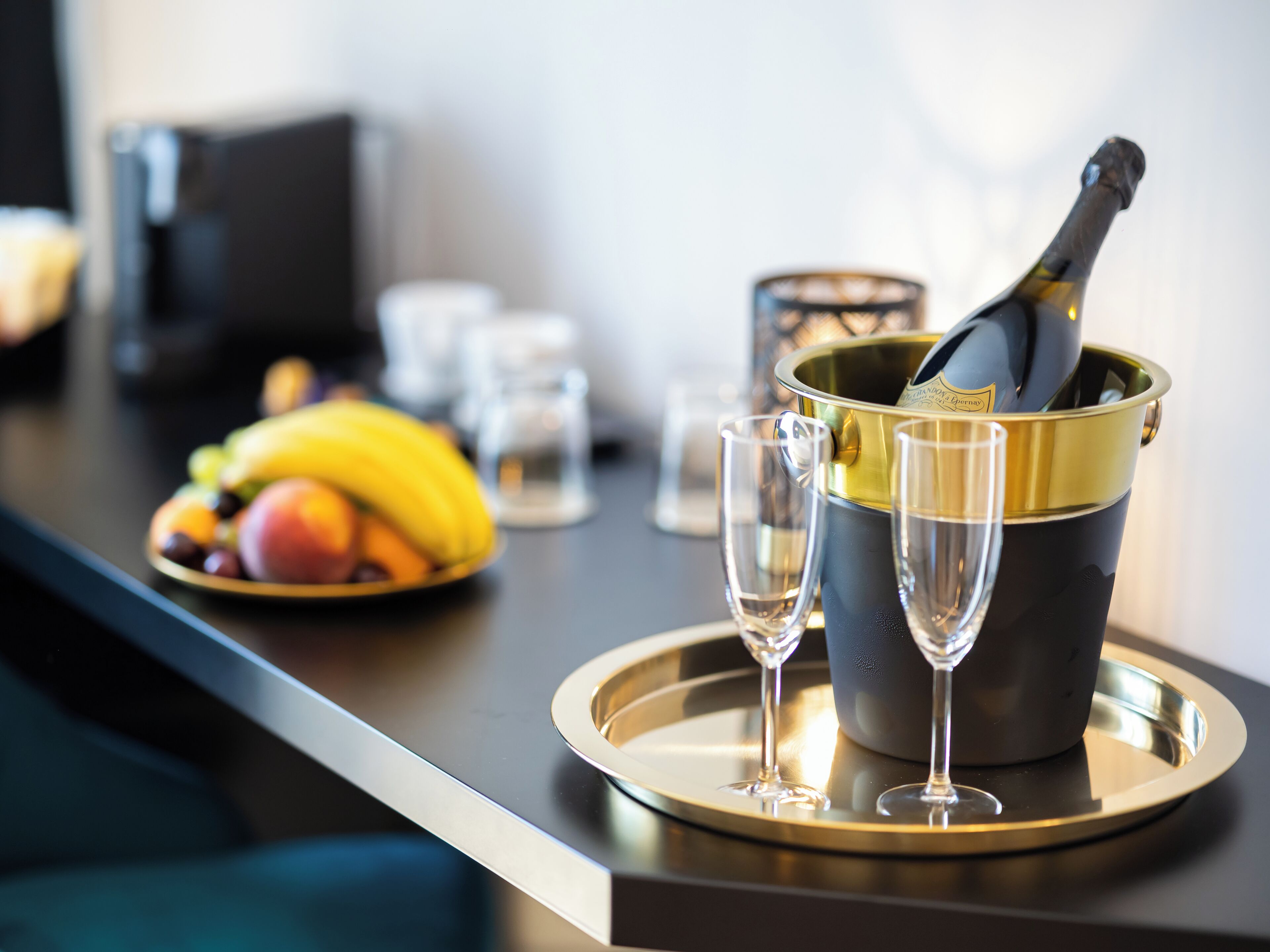 A champagne bucket with two glasses on a tray, a plate of fruit, and a bottle of champagne.