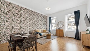 Una sala de estar moderna con comedor, con papel tapiz estampado, suelo de madera, un sofá, una mesa de centro y una mesa de comedor lista para cuatro personas.