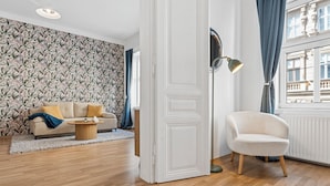 Una sala de estar con un papel tapiz estampado, un sofá, una mesa de centro, una silla y un ventanal con cortinas.
