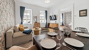 Una sala moderna con un sofá, una mesa de comedor para cuatro personas y un televisor montado en la pared.