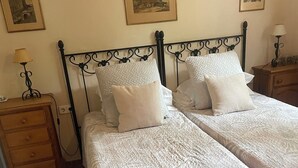 Een slaapkamer met twee bedden, een houten nachtkastje, een lamp en lijstjes met foto's aan de muur.