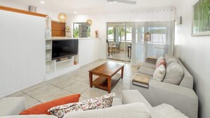 A modern living room with a flat-screen TV, a wooden coffee table, a sofa, and a ceiling fan. - Elevated Resort-style Terrace near Botanic Gardens (Cairns North)