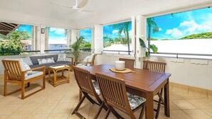 A dining area with a wooden table and chairs, a ceiling fan, and large windows with a view of a beach. - Elevated Resort-style Terrace near Botanic Gardens (Cairns North)