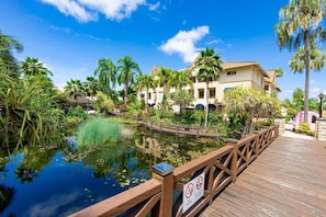 A resort with a wooden deck, a pond, and palm trees.
