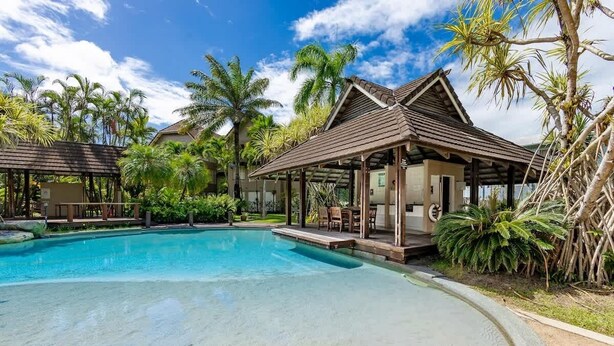 A swimming pool with a wooden deck and lounge chairs, surrounded by palm trees and a clear sky. - Elevated Resort-style Terrace near Botanic Gardens (Cairns North)