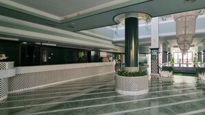 Een ruime lobby met een zwart-wit vloertegelpatroon, een centrale kolom met een plantenbak en een moderne kroonluchter.