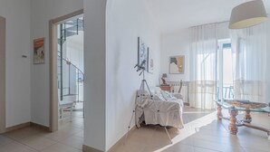 Un vaste espace de vie comprenant une table à manger en verre, un trépied et un lit recouvert d’une couverture blanche.