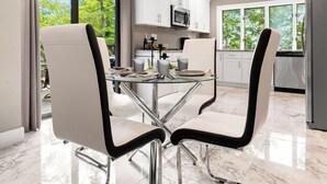 Une cuisine moderne avec des meubles blancs, une table à manger en verre et deux chaises recouvertes d’un tissu noir et blanc.