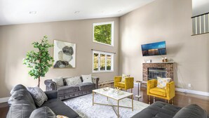 Un salon moderne avec un canapé d’angle, un fauteuil jaune, une cheminée et une grande fenêtre.
