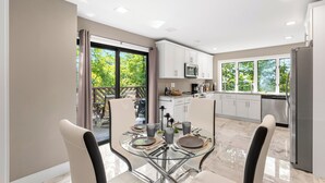 Une cuisine moderne avec des meubles blancs, un réfrigérateur en acier inoxydable et un coin repas comprenant une table et des chaises en verre.