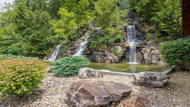 A waterfall cascading over rocks, surrounded by lush greenery and a small pond. - Evergreen Oasis - 6BR, Theater Room & 2 Hot Tubs!! (Sevierville)