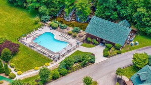 An aerial view of a property with a swimming pool, lounge chairs, and a building with a green roof. - Evergreen Oasis - 6BR, Theater Room & 2 Hot Tubs!! (Sevierville)