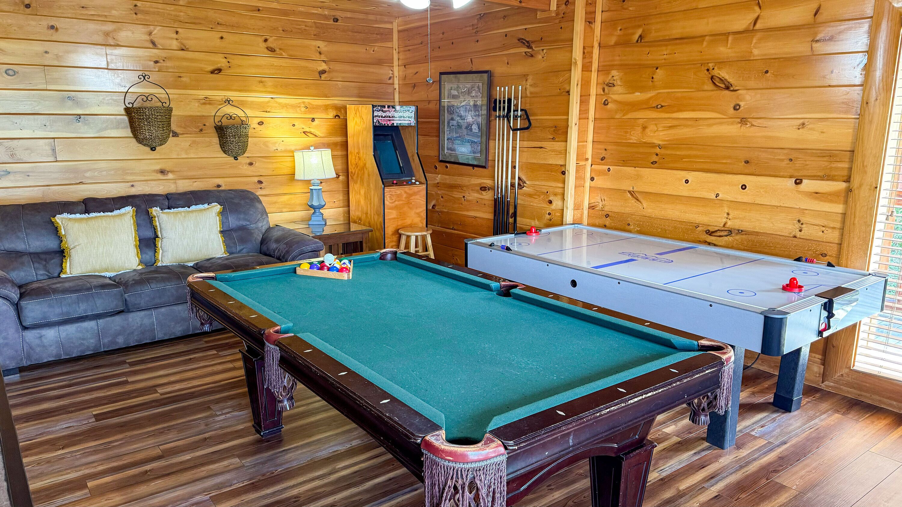 Une pièce chaleureuse avec une table de billard, un canapé avec des coussins, une lampe et un tableau encadré au mur.