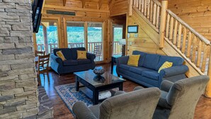A cozy log cabin interior with two sofas, a coffee table, and a staircase. - Evergreen Oasis - 6BR, Theater Room & 2 Hot Tubs!! (Sevierville)