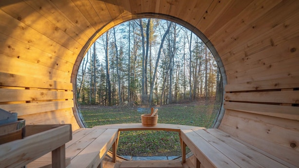 Una cabaña de madera con un ventanal circular, bancos de madera y una pequeña mesa con una cesta.
