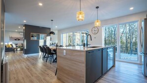 Una cocina moderna con una isla central, ventanas amplias y una zona de comedor con sillas y una mesa.