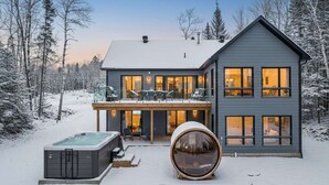 Una casa moderna de dos pisos con balcón, jacuzzi y un objeto cilíndrico grande en primer plano.