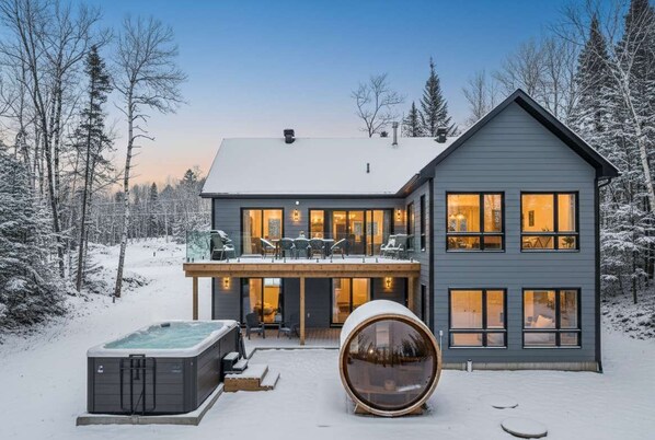 Une maison moderne à deux étages, dotée d’un balcon, d’un jacuzzi et d’un grand objet cylindrique placé au premier plan.