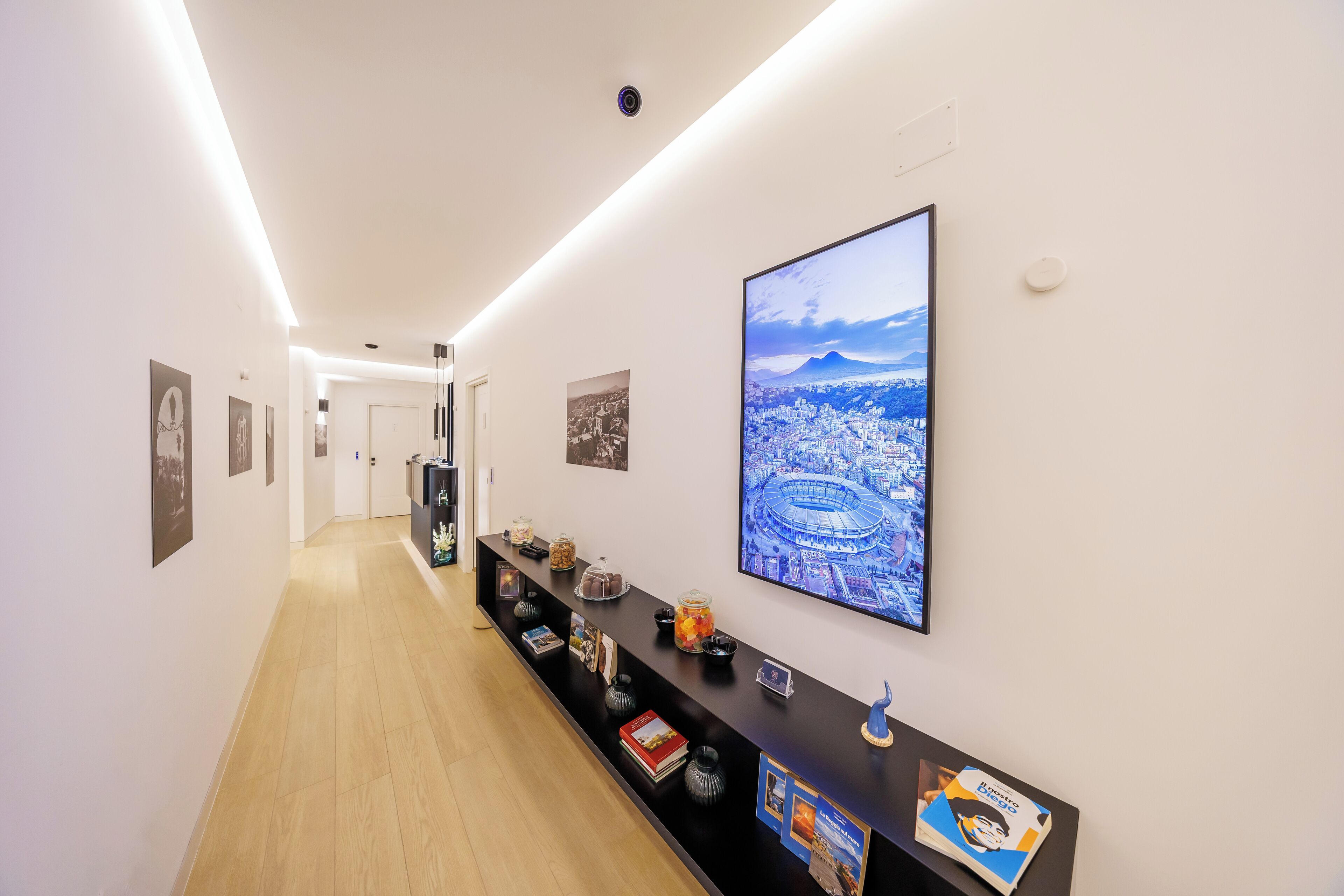 A hallway with a long reception desk, framed photographs, and a large cityscape painting.